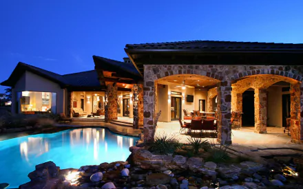 HD desktop wallpaper of an elegant stone house with illuminated interiors and a serene pool at dusk.
