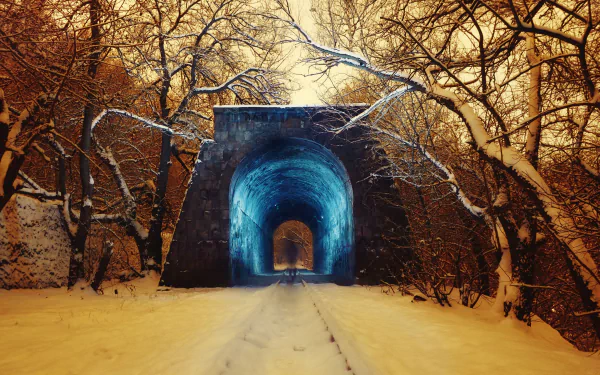 4K Ultra HD winter photography of a snow-covered train track leading through a glowing blue tunnel, framed by bare trees under a golden sky.