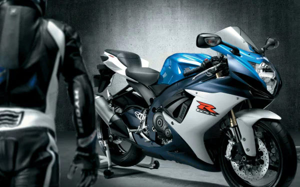HD PC desktop wallpaper/background of a blue-and-white Suzuki GSXR sport vehicle parked in a concrete garage, a rider in leathers partially visible in the foreground.