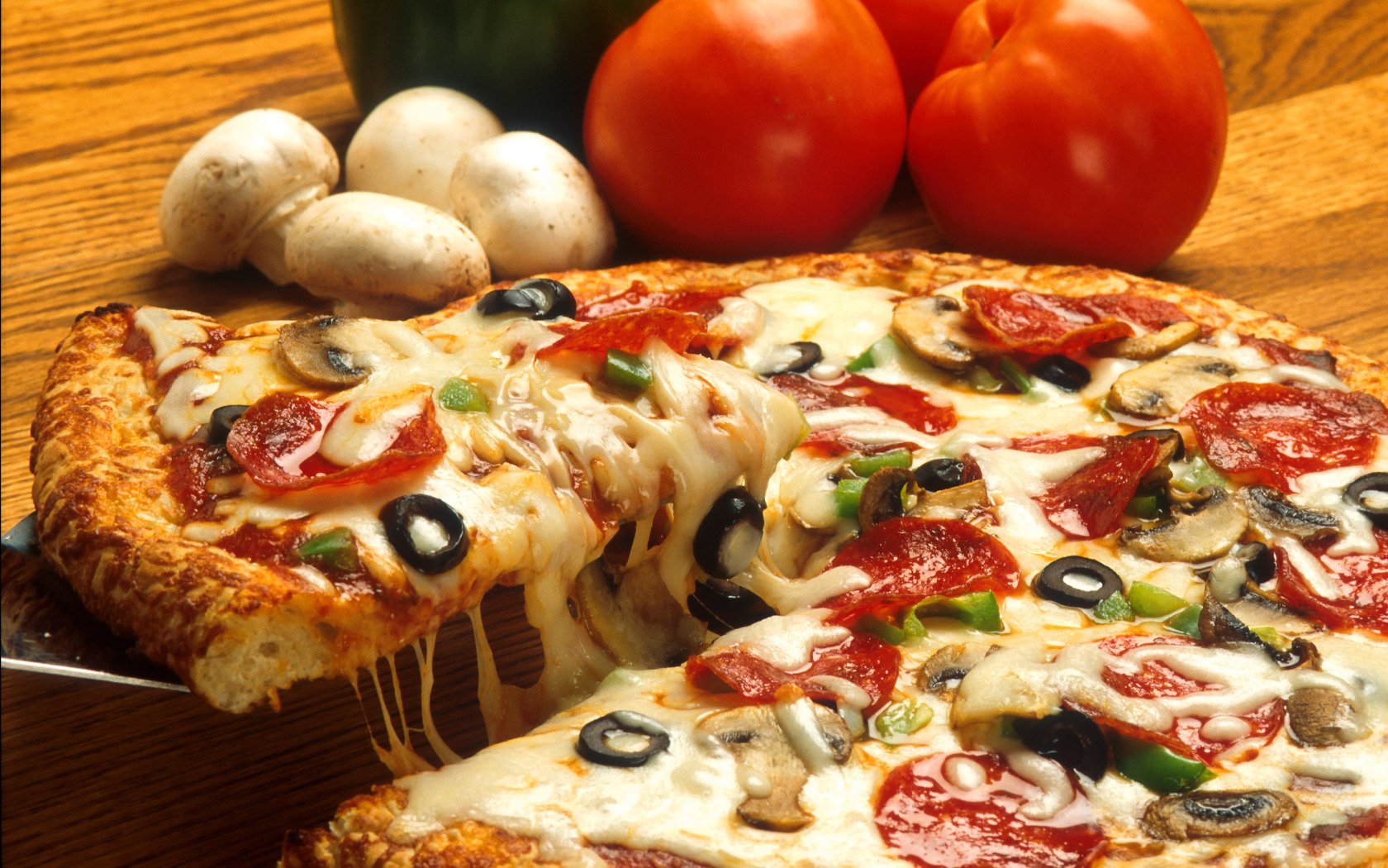 HD PC desktop wallpaper featuring a close-up of a freshly baked pizza with pepperoni, mushrooms, olives, and tomatoes in the background.
