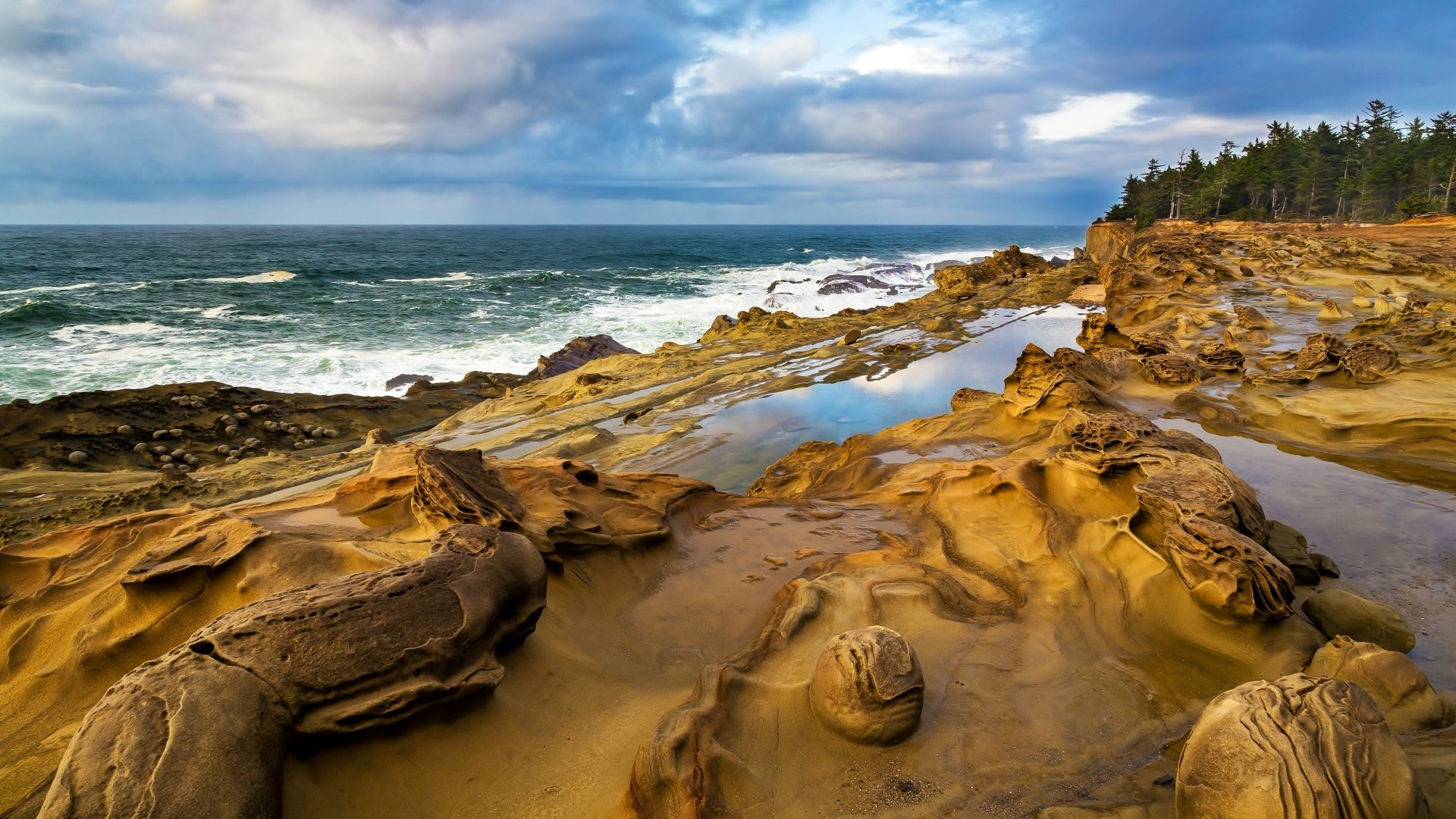 4K Ultra HD PC desktop wallpaper of a rugged coastline with rocky shore, shallow tidal pools, and a partly cloudy sky over the ocean, showcasing natural coastal beauty.
