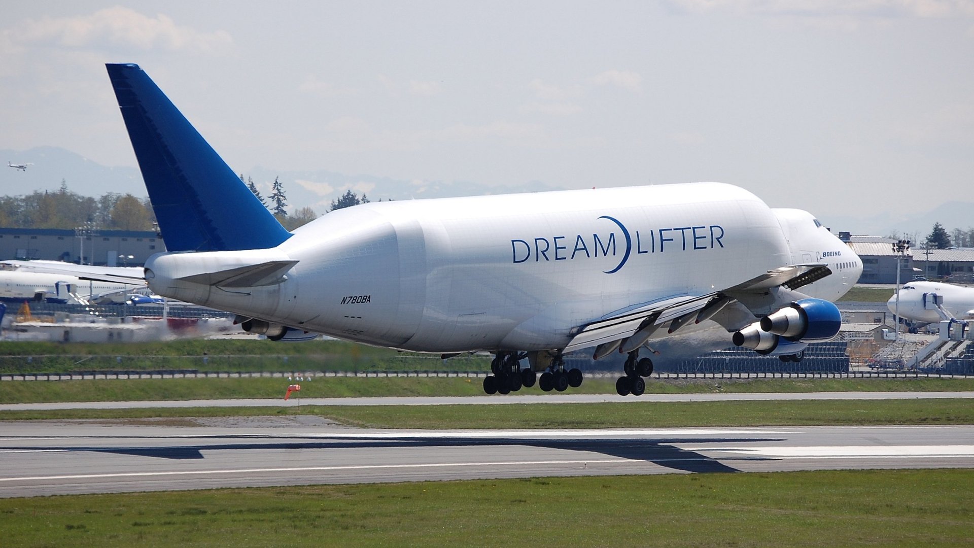 Boeing 747 Dreamlifter cargo vehicle touching down on runway, Dreamlifter livery visible — 2K Quad HD PC desktop wallpaper background.