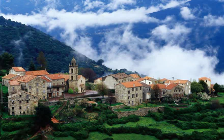 A scenic view of the village of Aregno in Corsica, France, featuring traditional stone buildings with orange roofs nestled among green hills and misty clouds.