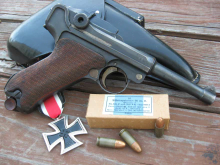 HD PC desktop wallpaper showing a man-made Luger pistol with holster, spare rounds and military medals arranged on a weathered wooden surface