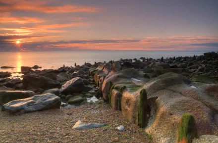 HD PC desktop wallpaper and background: rocky shoreline at sunset, golden sky reflecting on calm sea, moss-covered boulders in the foreground — tranquil nature scene.