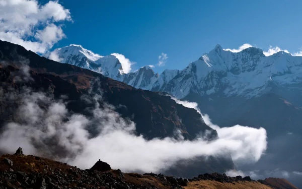 4K Ultra HD desktop wallpaper showcasing the majestic Himalayan mountains with clear blue skies, rugged peaks, and drifting clouds enveloping the natural landscape.
