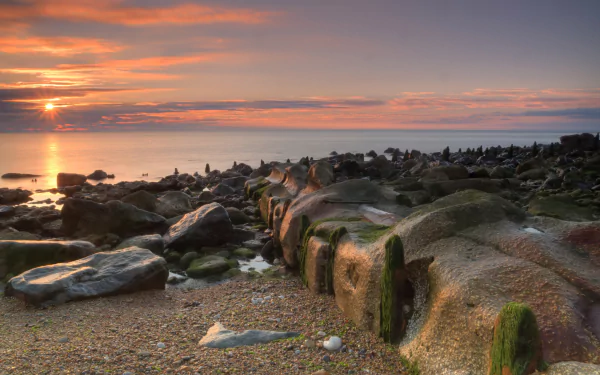 HD PC desktop wallpaper and background: rocky shoreline at sunset, golden sky reflecting on calm sea, moss-covered boulders in the foreground — tranquil nature scene.