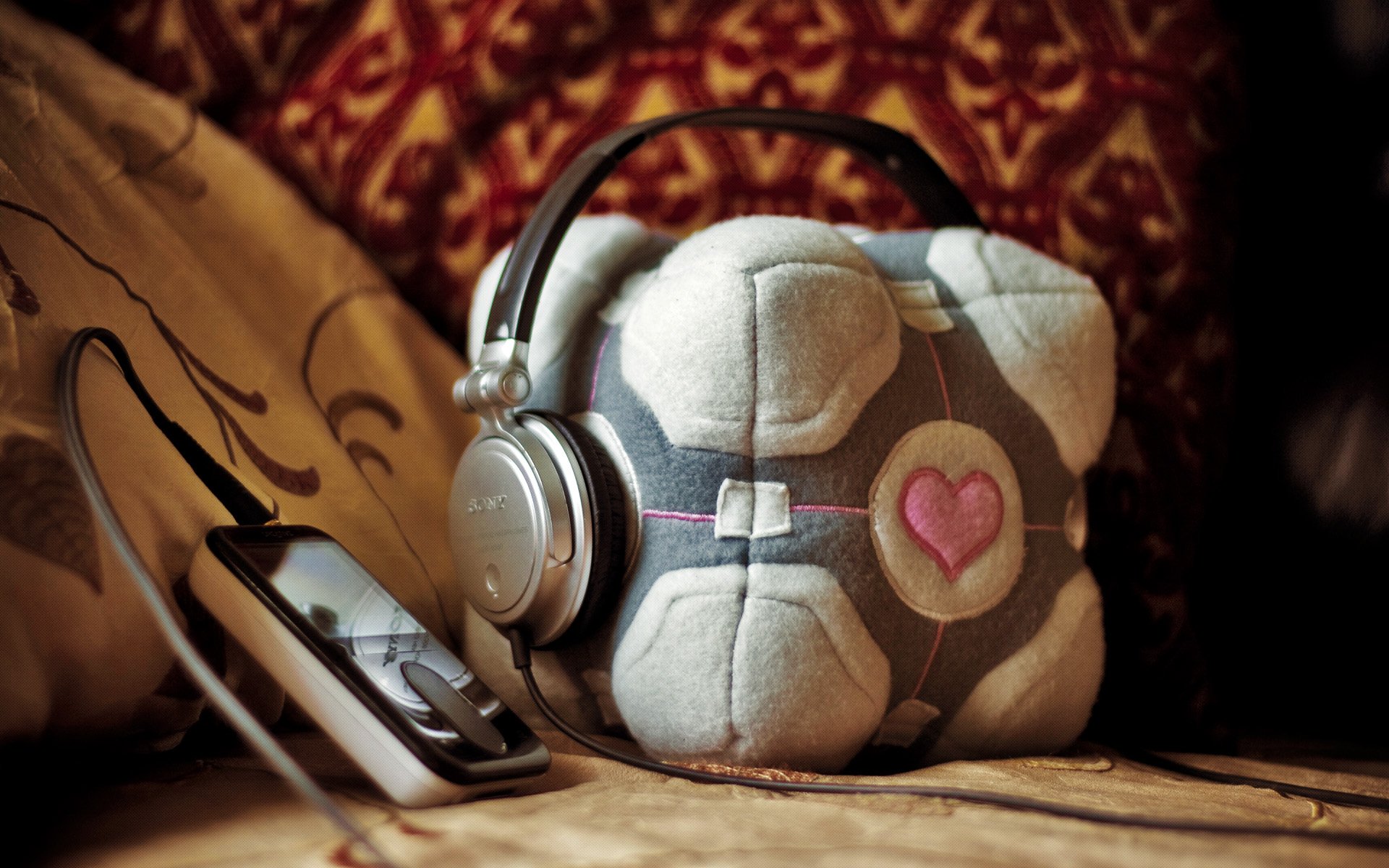 A cozy setup featuring a plush Companion Cube with headphones resting on it, alongside a music player, capturing the essence of Portal (Video Game) in HD wallpaper style.