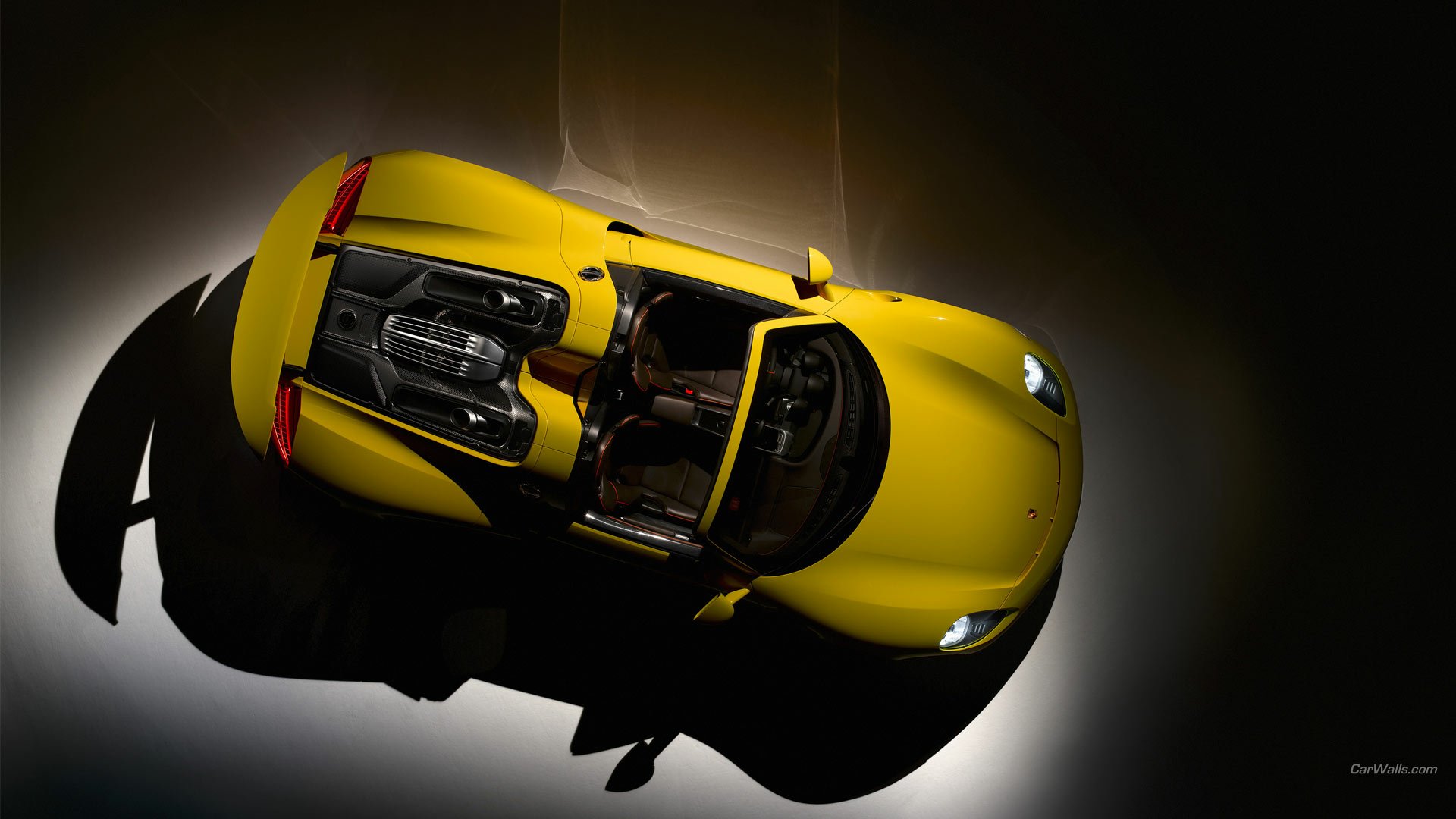 HD PC desktop wallpaper showing a top-down view of a yellow Porsche 918 Spyder sports car with open cockpit, lit by a dramatic spotlight against a dark background.