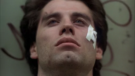 HD PC desktop wallpaper: close-up of a young man lying with a cheek bandage, cinematic, disco-era mood evoking Saturday Night Fever and the Tony Manero character.