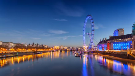 A stunning view of the London Eye illuminated at night, reflecting in the river, showcasing the vibrant lights of the surrounding buildings in a picturesque urban scene.
