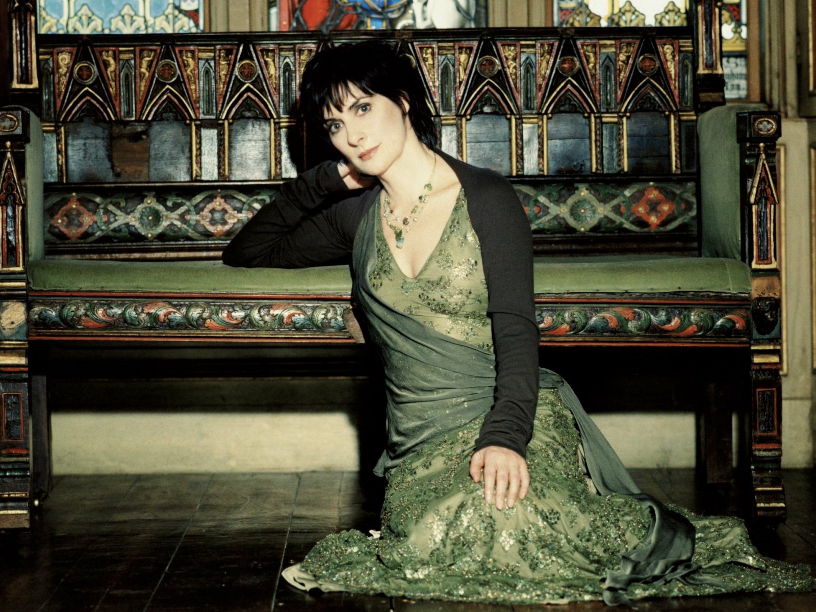 HD PC desktop wallpaper of a music singer in a flowing green gown seated on an ornate wooden bench, moody lighting and Celtic‑inspired atmosphere.
