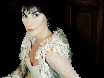 HD PC desktop wallpaper featuring a close-up portrait of Enya, with soft lighting highlighting her face and textured, light-colored clothing.