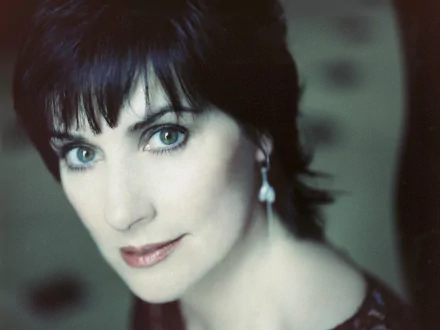 HD PC desktop wallpaper — close-up portrait of a female music singer with short dark hair, blue-green eyes and a dangling earring, bathed in soft, ethereal light.