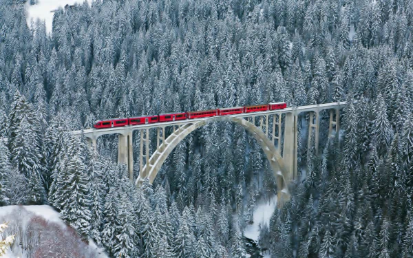 Red train crossing the man-made Langwieser Viaduct above a snow-covered Swiss forest — HD desktop wallpaper/background