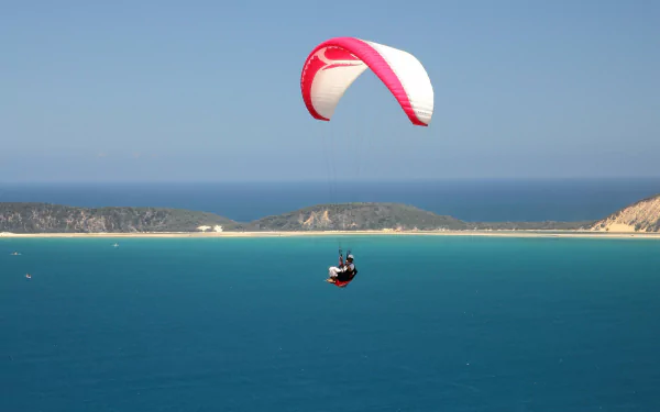 A paraglider soars above a vast blue ocean with distant cliffs under a clear sky, captured in stunning 4K Ultra HD as a dynamic sports desktop wallpaper.