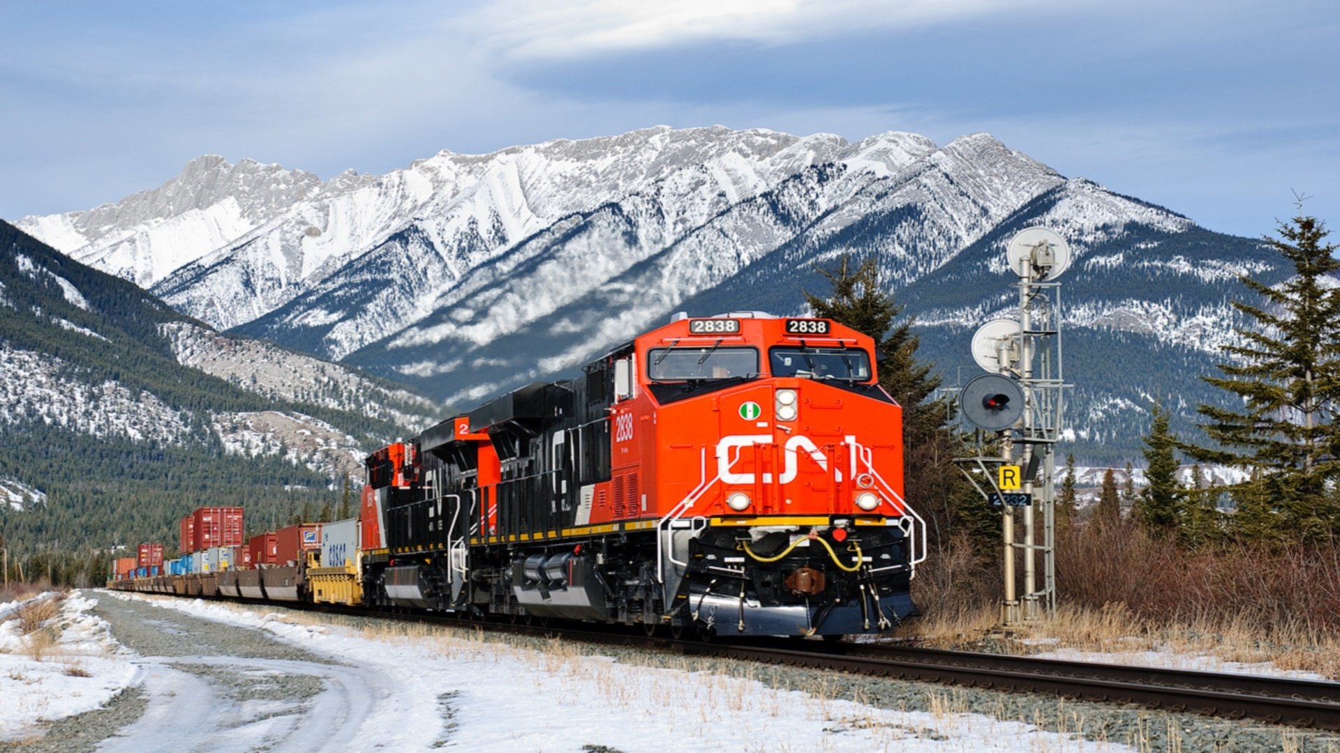 HD desktop wallpaper of a bright red Canadian train traveling through a snowy mountain landscape under a clear blue sky.