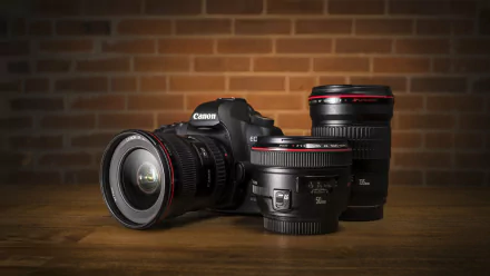 A Canon camera with two lenses is displayed on a wooden surface, set against a brick background, capturing a sleek, man-made design in stunning 4K Ultra HD resolution.