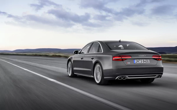 A sleek Audi A8 drives along an open road, showcasing its elegant design against a backdrop of expansive skies. This HD image serves as a stunning desktop wallpaper.