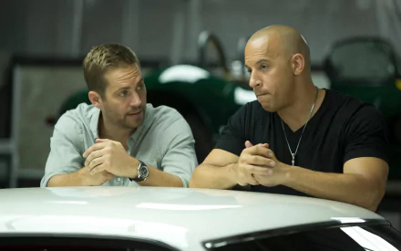 HD desktop wallpaper from Fast & Furious 6 featuring actors Vin Diesel and Paul Walker as characters Dominic Toretto and Brian O'Conner, respectively, sitting and talking in a garage.