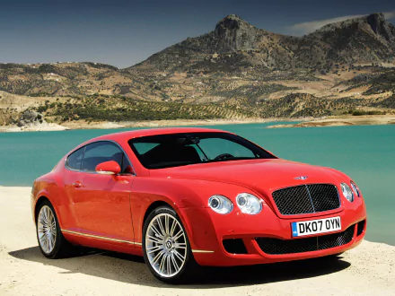 Red Bentley Continental GT Speed parked by a turquoise lakeside with rocky mountains in the background, showcased in an HD PC desktop wallpaper.