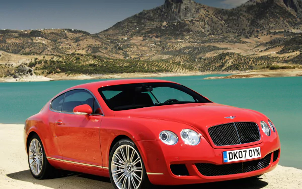Red Bentley Continental GT Speed parked by a turquoise lakeside with rocky mountains in the background, showcased in an HD PC desktop wallpaper.