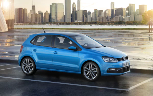 HD PC desktop wallpaper featuring a blue Volkswagen Polo parked by a waterfront with a city skyline in the background during sunset.