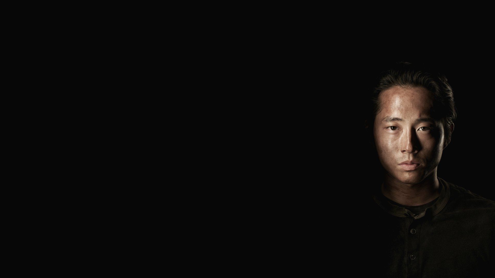 A dark, atmospheric image from the TV show The Walking Dead, featuring a close-up of a character's face, set against a black background, emphasizing a sense of tension.