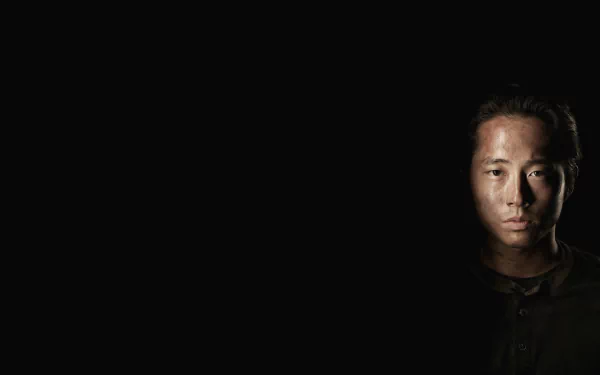 A dark, atmospheric image from the TV show The Walking Dead, featuring a close-up of a character's face, set against a black background, emphasizing a sense of tension.