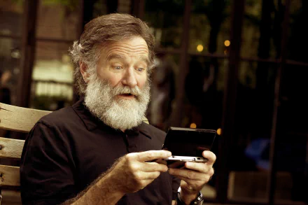 HD desktop wallpaper featuring a person resembling Robin Williams looking at a handheld device with an amused expression while seated on a bench.