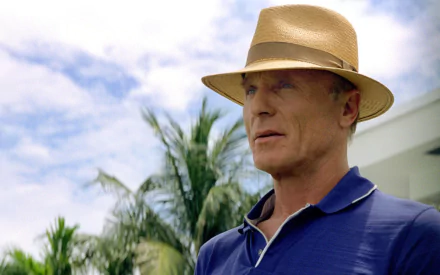 Ed Harris as Ed Dubois in Pain & Gain, featuring a close-up with a straw hat and palm trees in the background, capturing a vibrant, cinematic moment.