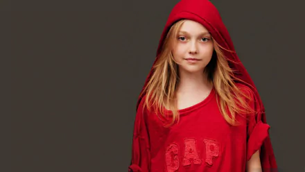 A striking HD wallpaper featuring Dakota Fanning, an American actress, wearing a red hoodie, exuding a confident and youthful vibe against a simple gray background.