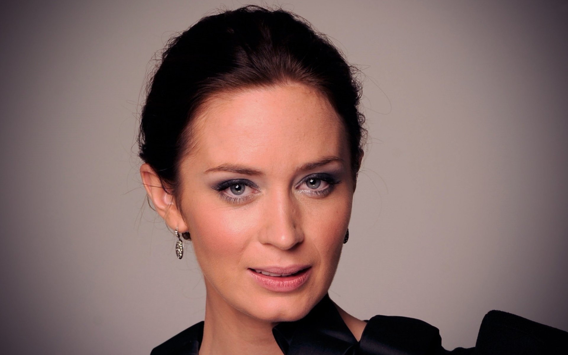 HD desktop wallpaper featuring English actress and celebrity Emily Blunt with a soft smile and elegant look against a neutral background.