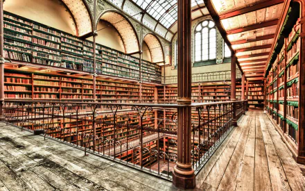 HD desktop wallpaper of a beautifully designed man-made library interior with wooden floors, iron railings, and tall bookshelves under arched windows and a glass ceiling.