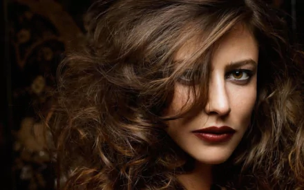 Close-up portrait of French actress Anna Mouglalis with voluminous hair and intense gaze, featured in a high-definition desktop wallpaper background.