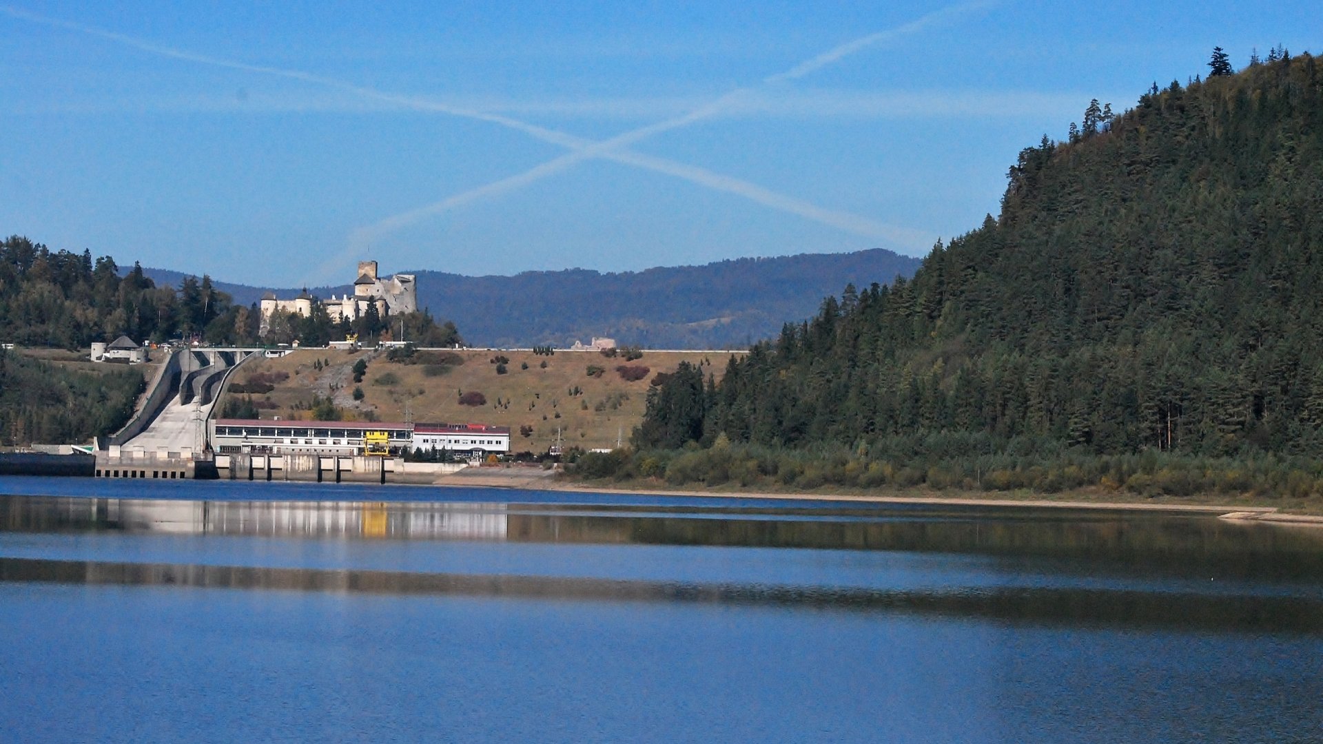 HD desktop wallpaper featuring the man-made Niedzica Castle overlooking a serene lake surrounded by forested hills under a clear blue sky.