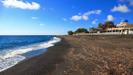 4K Ultra HD wallpaper of a black sand beach in Santorini, Greece, featuring calm blue waters and man-made structures along the shore under a bright sky.