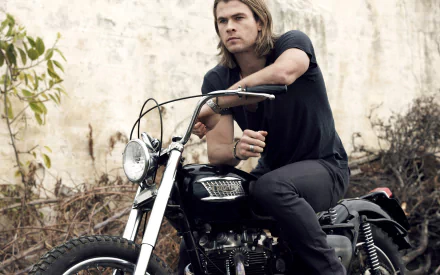 Chris Hemsworth, the Australian actor, poses confidently on a motorcycle against a rustic backdrop in this striking HD desktop wallpaper.