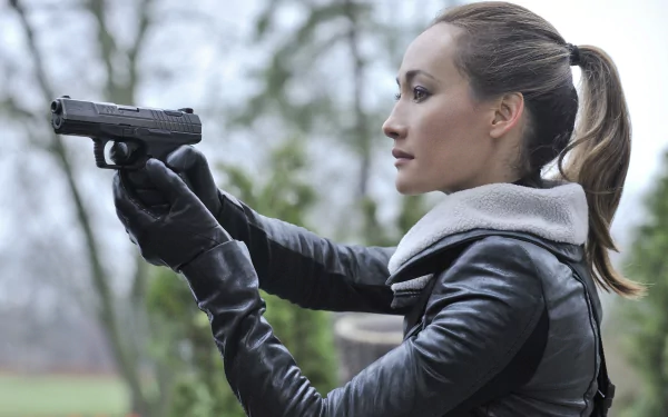 HD desktop wallpaper featuring Maggie Q as Nikita from the TV show, aiming a handgun with focus and determination in an outdoor setting.