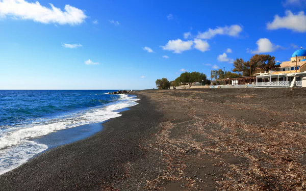 4K Ultra HD wallpaper of a black sand beach in Santorini, Greece, featuring calm blue waters and man-made structures along the shore under a bright sky.