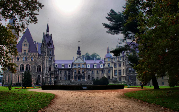HD desktop wallpaper featuring the man-made Moszna Castle framed by trees under a cloudy sky.
