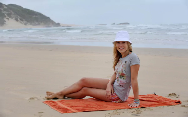 German actress Wolke Hegenbarth sits smiling on an orange towel at a serene beach, featured in an HD PC desktop wallpaper and background.