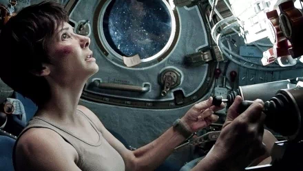 A dramatic scene from the movie Gravity (2013), featuring a woman in a spacecraft, focused on her controls as she gazes out at the vastness of space through the window.