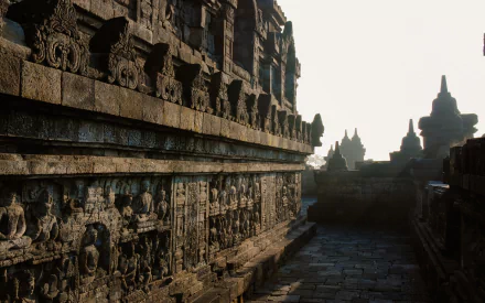 HD desktop wallpaper of Borobudur temple showcasing intricate religious stone carvings bathed in soft, natural light with silhouetted stupas in the background.