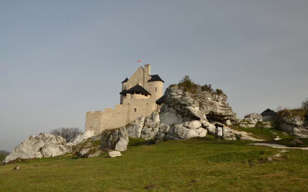 HD PC desktop wallpaper background of Bobolice Castle, a man-made stone fortress perched on rocky crags with a grassy foreground beneath a pale sky.