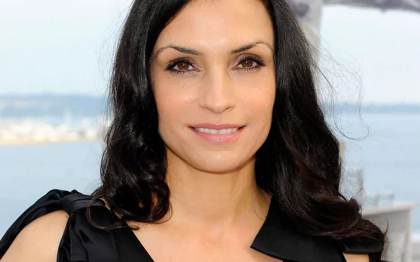 HD desktop wallpaper of Dutch actress Famke Janssen smiling with a scenic blurred waterfront background.