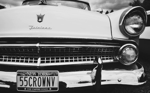 Black and white HD desktop wallpaper featuring a close-up of the front grille and headlights of a classic Ford Fairlane with a New York license plate.