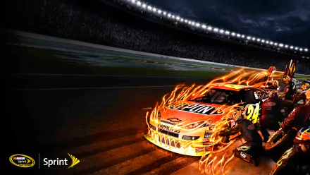 HD PC desktop wallpaper: NASCAR stock car with blazing flame graphics racing under stadium lights while pit crew works — sports background.