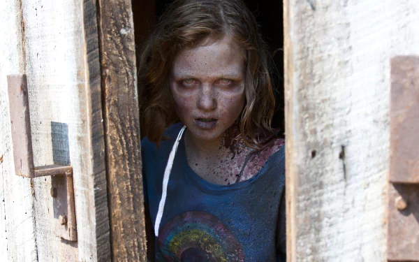 A chilling moment from the TV show The Walking Dead, featuring a disheveled girl with a haunting gaze, peering through a wooden door, capturing the eerie essence of the series.