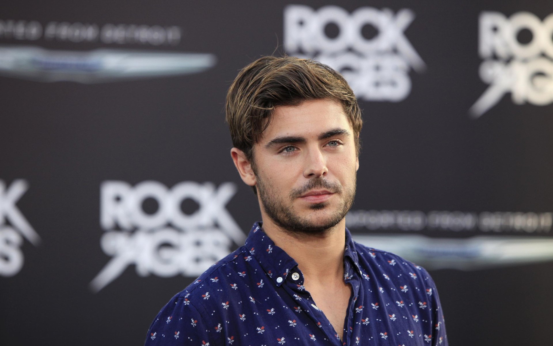 HD PC desktop wallpaper featuring American actor and celebrity Zac Efron against a blurred event backdrop.